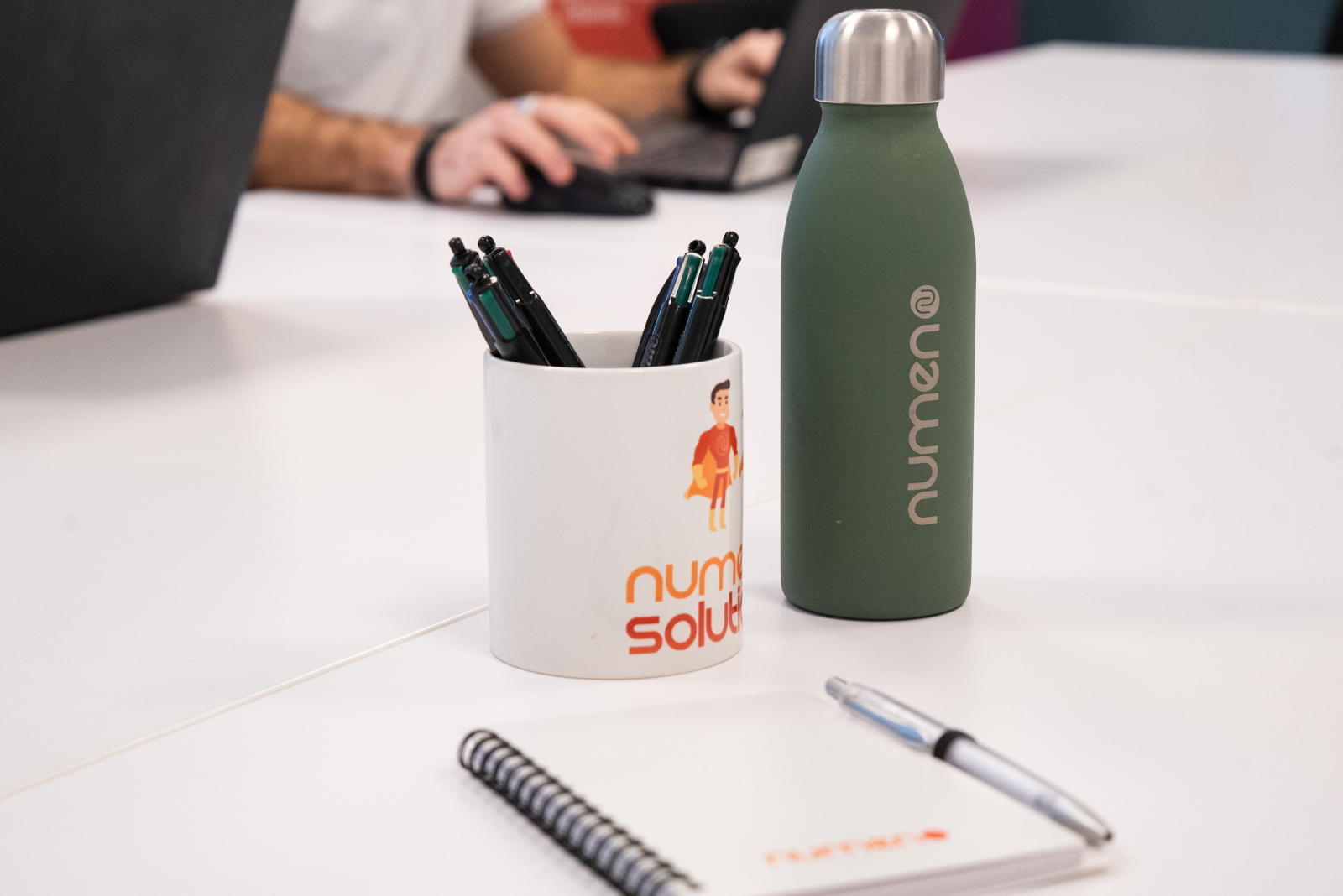 Nous recrutons de nouveaux salariés Numen. Image d'une tasse, un carnet, des stylos et une gourde à l'image de Numen. Tous les objets sont logotés aux couleurs de Numen