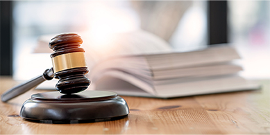 Numen répond aux exigences réglementaires et assure une gestion documentaire sécurisée et conforme. Image d'un marteau de la justice placé à côté d'un livre ouvert.