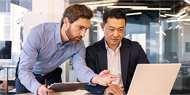 Avoir une gestion documentaire optimisée vour permet des bénéfices économiques et organisationnels. Image de deux hommes devant un ordinateur. L'un montre quelque chose sur l'écran à l'autre.