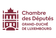 Témoignage client - Chambre des Députés du Luxembourg. Un projet de numérisation d'archives parlementaires. Image d'une femme dans une bibliothèque consultant une grosse archive avec un stylo à la main. Elle est entourée de papiers anciens, de livres précieux et devant une bibliothèque d'ouvrages précieux protégés sous verre.